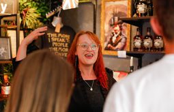 A costumed guide at Villains Rum of York leads a rum tasting inside a dimly lit shop filled with vintage decor and bottles. Guests smile and raise tasting glasses as they listen to stories of York’s historical villains.