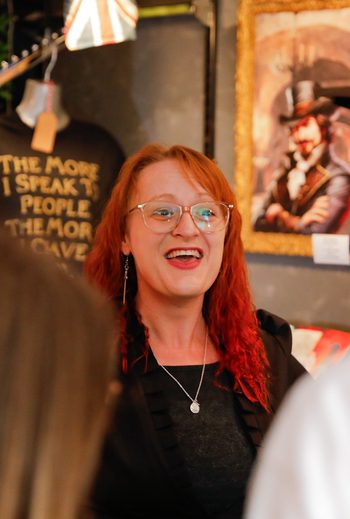 A costumed guide at Villains Rum of York leads a rum tasting inside a dimly lit shop filled with vintage decor and bottles. Guests smile and raise tasting glasses as they listen to stories of York’s historical villains.